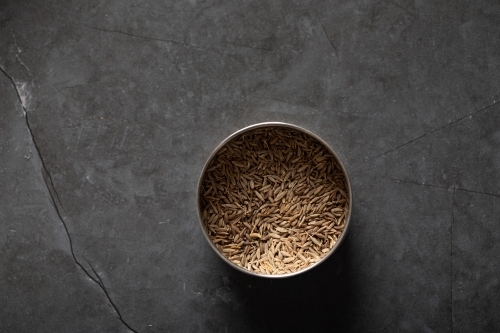 Spice tin of cumin seeds on dark marble background