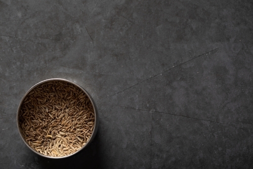 Spice tin of cumin seeds on dark marble background - Australian Stock Image