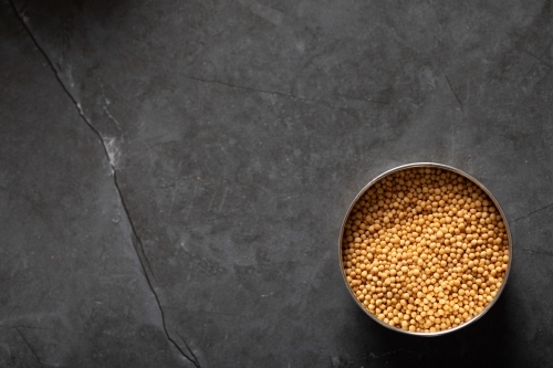 Spice tin of yellow mustards seeds on dark marble background - Australian Stock Image