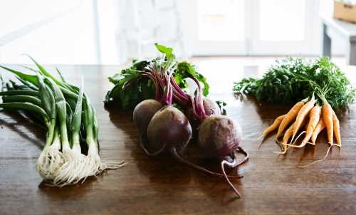 Spring onions, beetroot and carrots on a wooden kitchen bench - Australian Stock Image