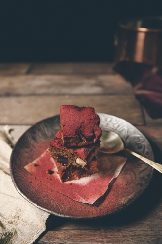 Stack of freshly baked red dusted chocolate brownies on timber surface with dark background - Australian Stock Image