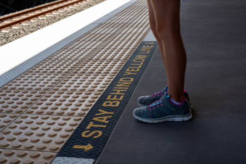 Stand behind the yellow line, girl in sneakers standing on a train platform - Australian Stock Image