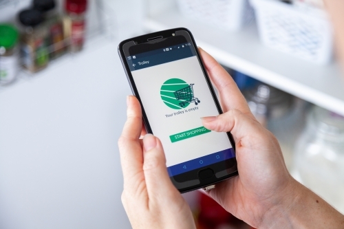 Start shopping - online grocery shopping app concept oh phone in front of pantry