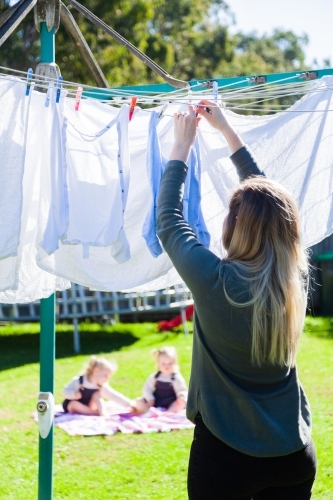 Stay at home mum hanging out washing in the backyard with kids picnic outside - Australian Stock Image