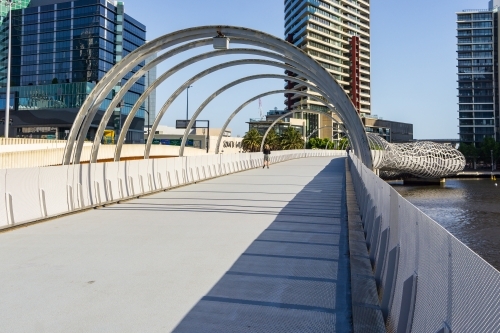 Steel arches over an elevated pedestrian bridge over a river - Australian Stock Image