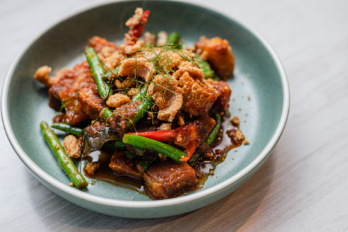 Stir-fried crackling pork belly, green beans, red peppers, and crispy garnishes - Australian Stock Image