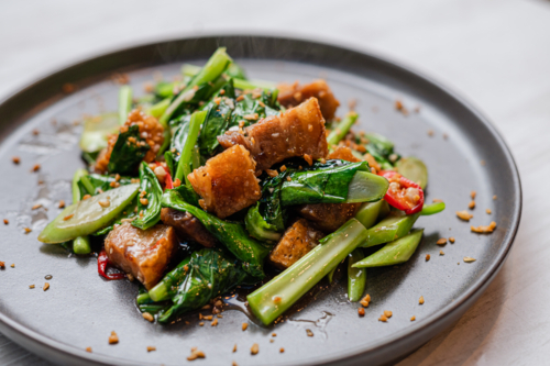 Stir-fried greens and crackling pork belly, with a sprinkle of sesame seeds - Australian Stock Image