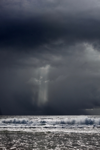 Storm behind ocean, surfer in distance, space above - Australian Stock Image