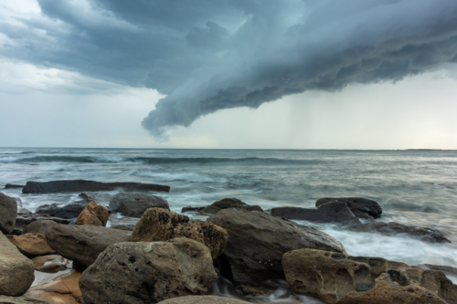 Storm clouds over ocean with rocky shoreline and waves - Australian Stock Image