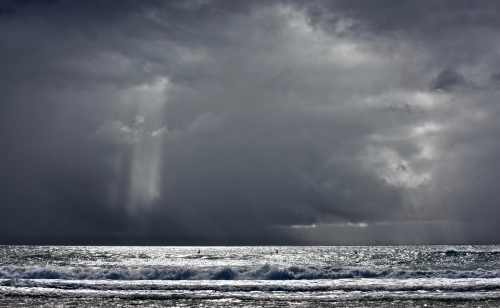 Storm over ocean, casting light, silver sea, moody - Australian Stock Image