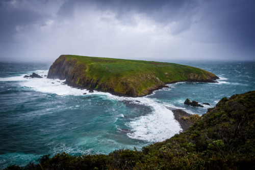 Stormy seas surround the rugged green slopes of Courts Island off the coast of Tasmania - Australian Stock Image