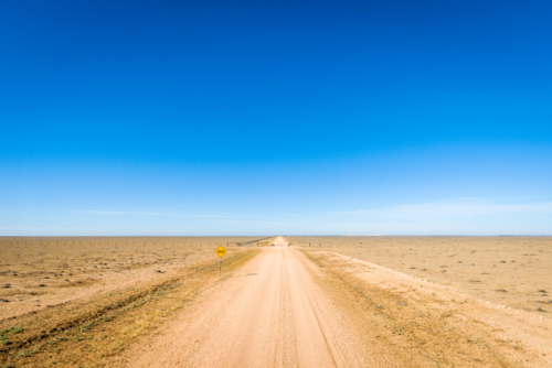 Straight dirt road through flat arid plains under clear blue sky - Australian Stock Image