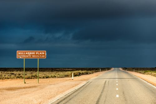 Straight road leading into the Nullarbor Plain under moody sky. - Australian Stock Image
