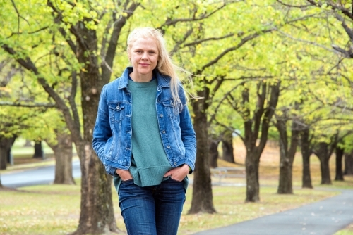 Strawberry blonde woman standing in front of a line of trees in winter. - Australian Stock Image