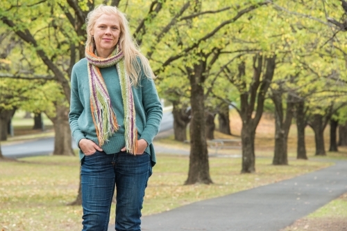 Strawberry blonde woman standing in front of a line of trees in winter wearing a scarf. - Australian Stock Image
