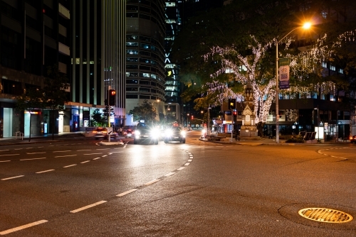 Street scene at night in Brisbane CBD with vehicles and light decorated tree - Australian Stock Image