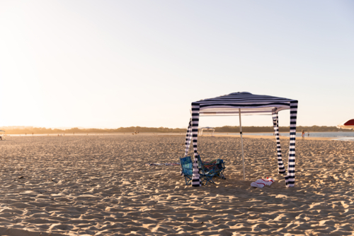 Striped navy‑and‑white canopy stands on the sandy shore - Australian Stock Image