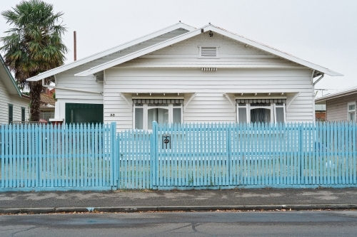 Suburban weatherboard house behind blue picket fence