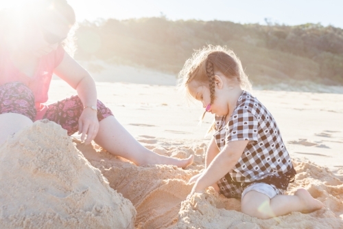 Sun flare over mother and child building a sandcastle on the beach - Australian Stock Image