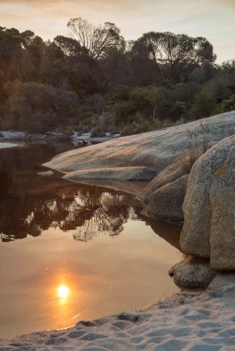 Sun reflection in still water surrounded by boulders on beach