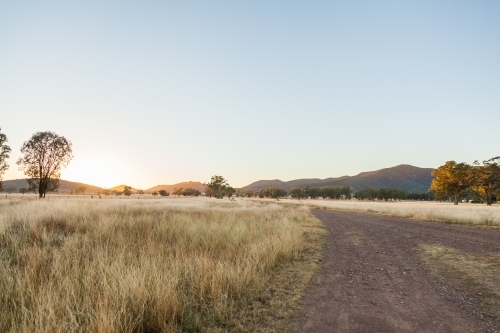 Sun rising up over paddock and dirt road on farm - Australian Stock Image