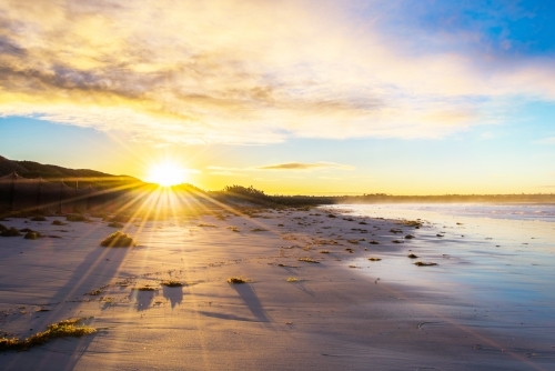 Sun shines over the land on a deserted beach. - Australian Stock Image
