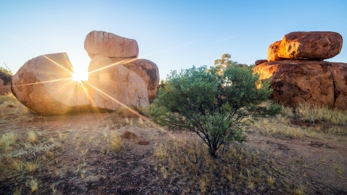 Sun shining through large boulder at sunrise - Australian Stock Image