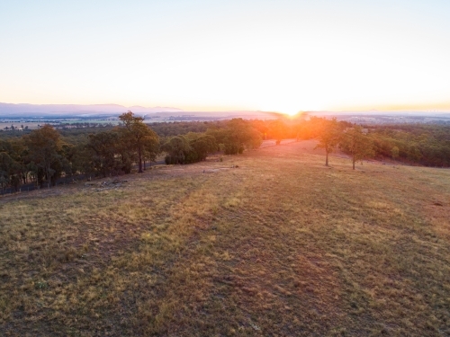 Sun sinking below the horizon of trees and empty paddock - Australian Stock Image