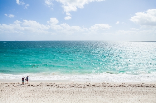 Sunlight on beach with distant people swimming in water and watching the waves - Australian Stock Image