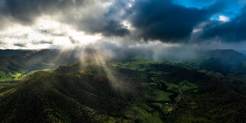 Sunlight piercing through the cloudy sky over the mountain terrain - Australian Stock Image