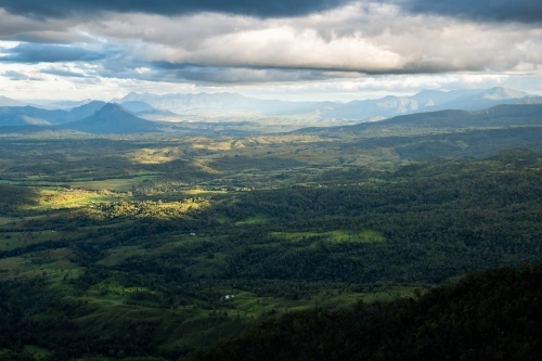 Sunlight piercing through the cloudy sky over the mountainous terrain. - Australian Stock Image