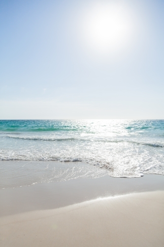 Sunlight sparkling on clear waters of the sea as waves wash the sand - Australian Stock Image