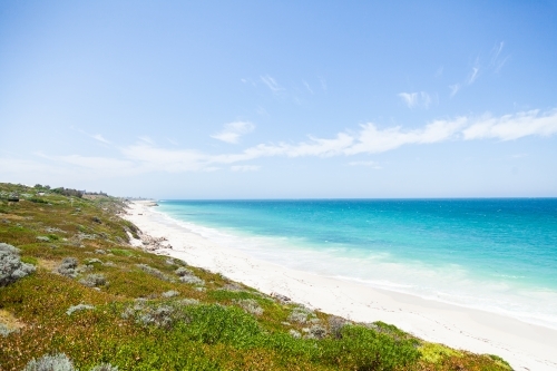 Sunlit coastland with view of shrubs, beach and clear blue coastal waters - Australian Stock Image
