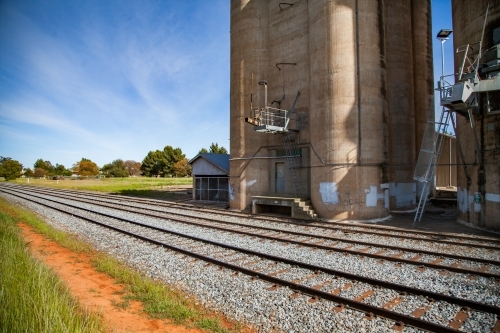 Sunlit train tracks running beside wheat silo infrastructure