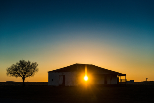 Sunrise behind an old outback building silhouetted on the horizon. - Australian Stock Image