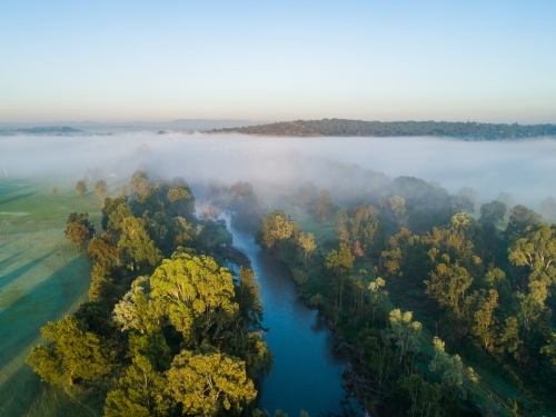 Sunrise light in morning touching treetops beside blue river in New South Wales Australia - Australian Stock Image