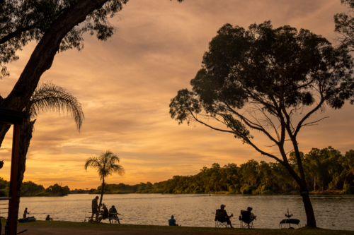 sunset at river with trees and water, people and ski boats silhouetted - Australian Stock Image