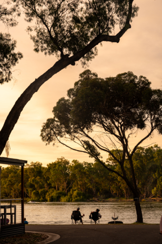 sunset at river with trees and water, people and ski boats silhouetted - Australian Stock Image