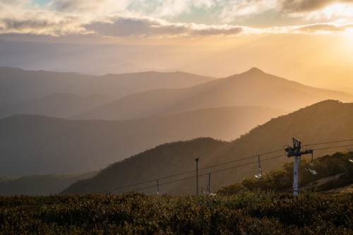 Sunset on Mt Buller with ski lift in shot and green foliage in foreground - Australian Stock Image