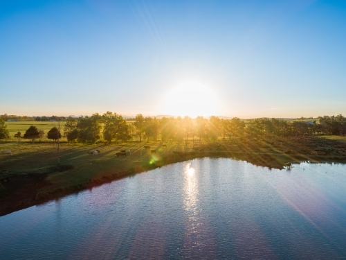 Sunset rays over water of farm dam with cattle in paddock - Australian Stock Image