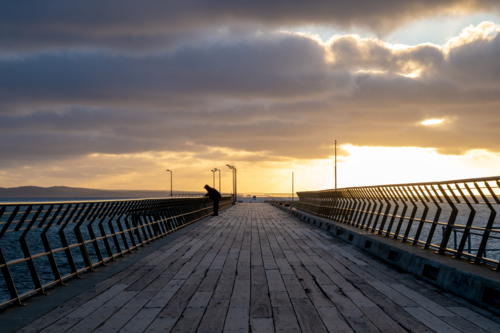 Sunset views along a wooden pier with a person silhouetted against the horizon. - Australian Stock Image
