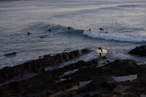 Surfer heading out off rocks in ocean on sunrise - Australian Stock Image