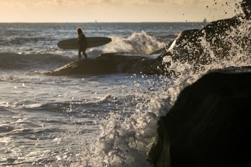 surfer on the rocks with crashing waves