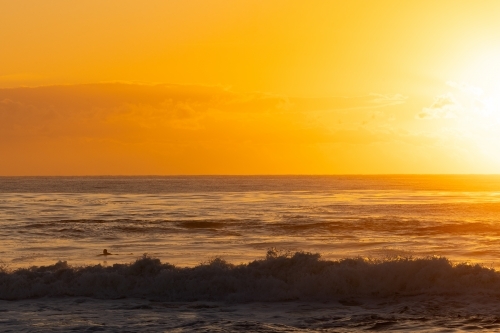 Surfer paddling out into vibrant yellow sunrise over the ocean at Brunswick Heads, NSW - Australian Stock Image