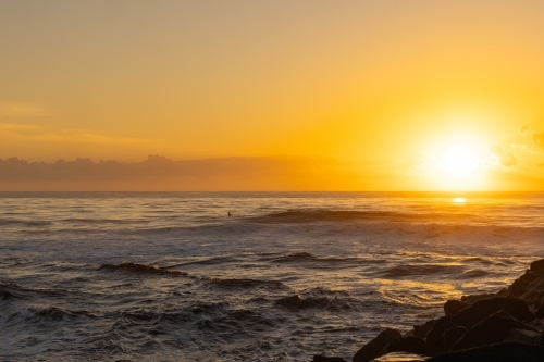 Surfer paddling out into vibrant yellow sunrise over the ocean at Brunswick Heads, NSW - Australian Stock Image