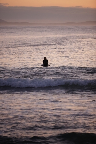 Surfer waiting for waves in ocean on sunrise - Australian Stock Image