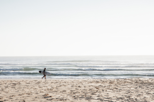 Surfer walking along beach in the early morning - Australian Stock Image