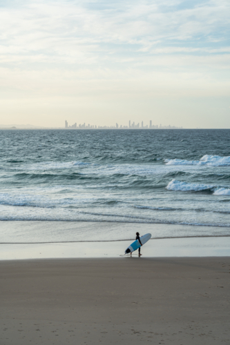 Surfer walking along the beach with surfing board - Australian Stock Image