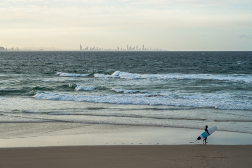 Surfer walking along the beach with surfing board - Australian Stock Image