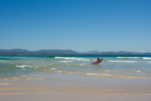 Surfer walking in water with pink surfboard - Australian Stock Image